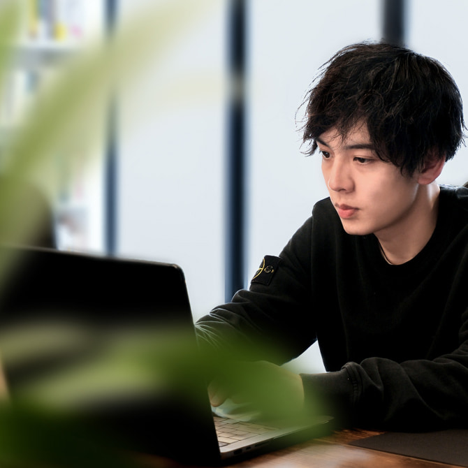 ノートパソコンで作業する男性社員。オフィスのデスクに座り、真剣な表情で画面を見つめている